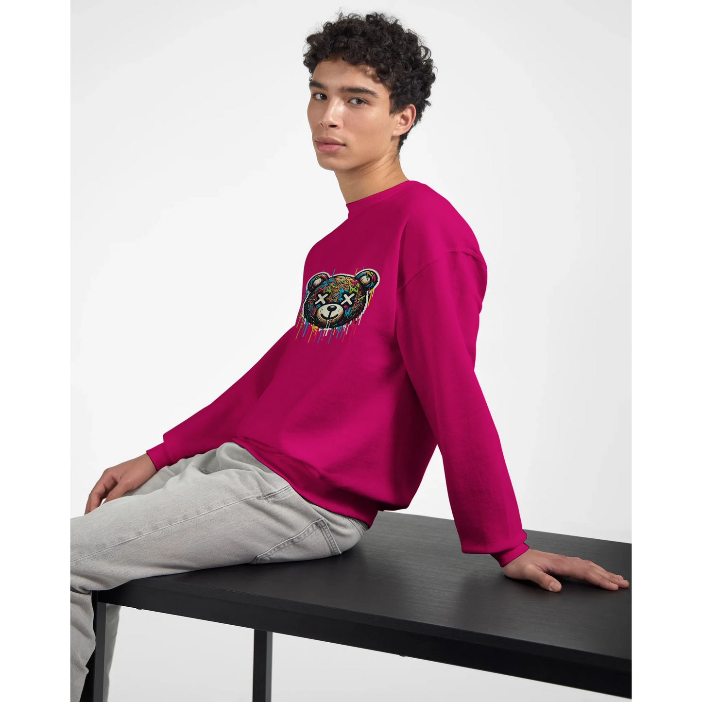 Person wearing a bright pink men's graphic sweatshirt with a colorful bear design, sitting on a black bench against a white background.