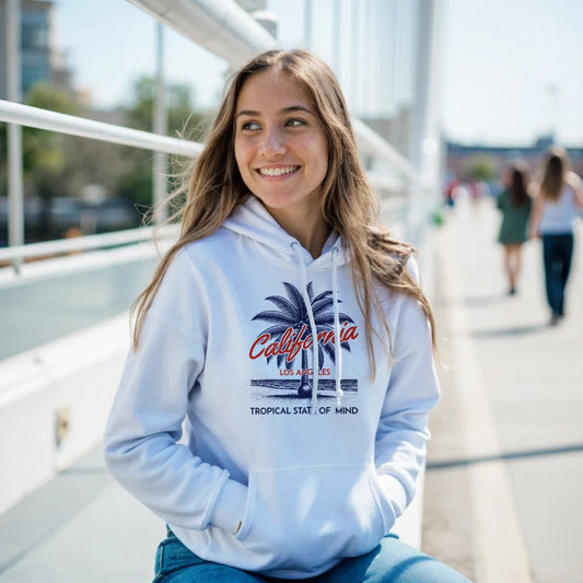 Woman wearing a white women’s hoodie with 'California' text, sitting outdoors on a sunny day.