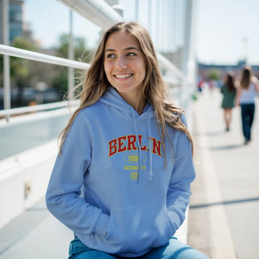 Woman wearing a blue women’s hoodie with 'BERLIN' printed on it, sitting outdoors.