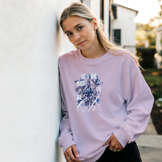 Young woman wearing a lavender Mental Health Jumper with blue floral graphic and 'It's OK Not to Be OK' text.