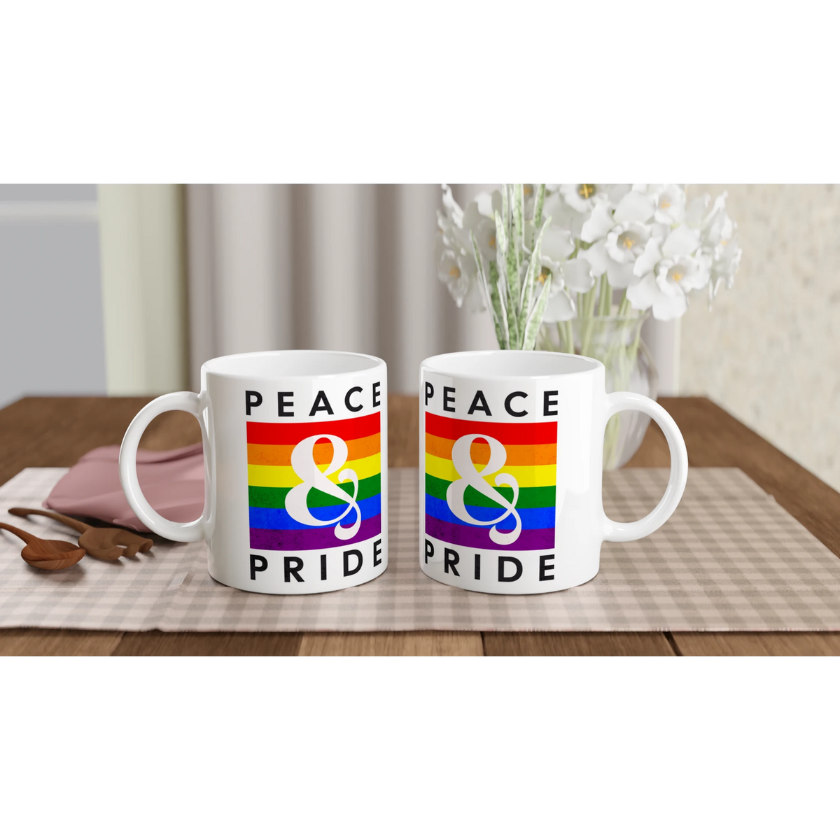 Two white mugs featuring rainbow 'PEACE & PRIDE' design on a table.