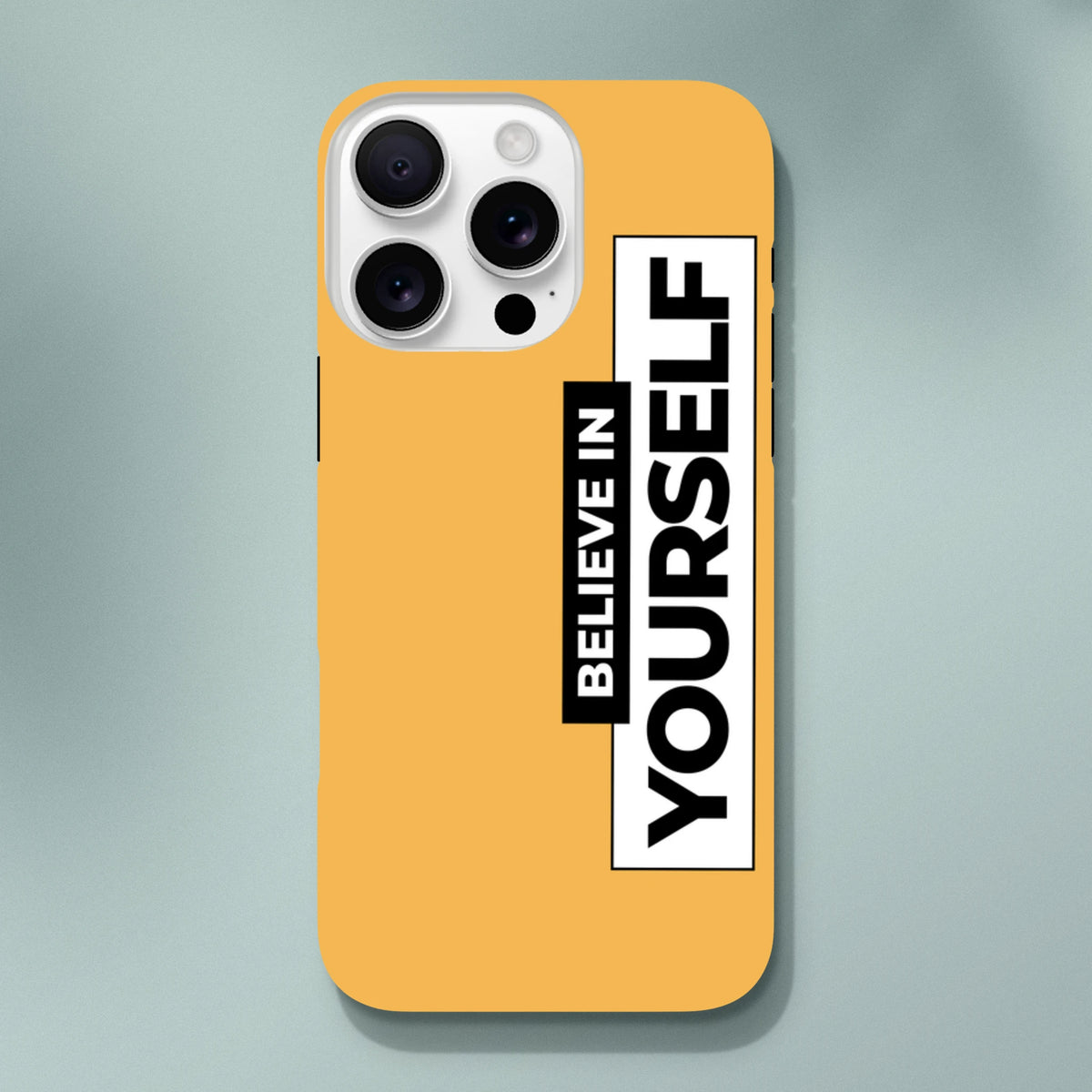 Orange iPhone case with vertical black and white "Believe In Yourself" slogan print. Tough phone cover for daily carry protection.