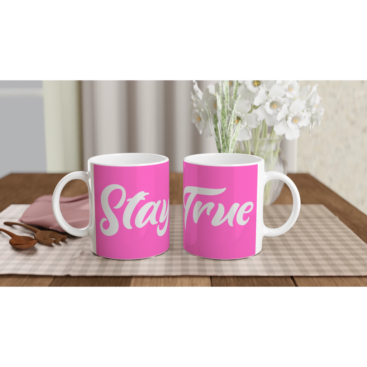 Two pink Stay True mugs with white cursive slogans on a wooden table.