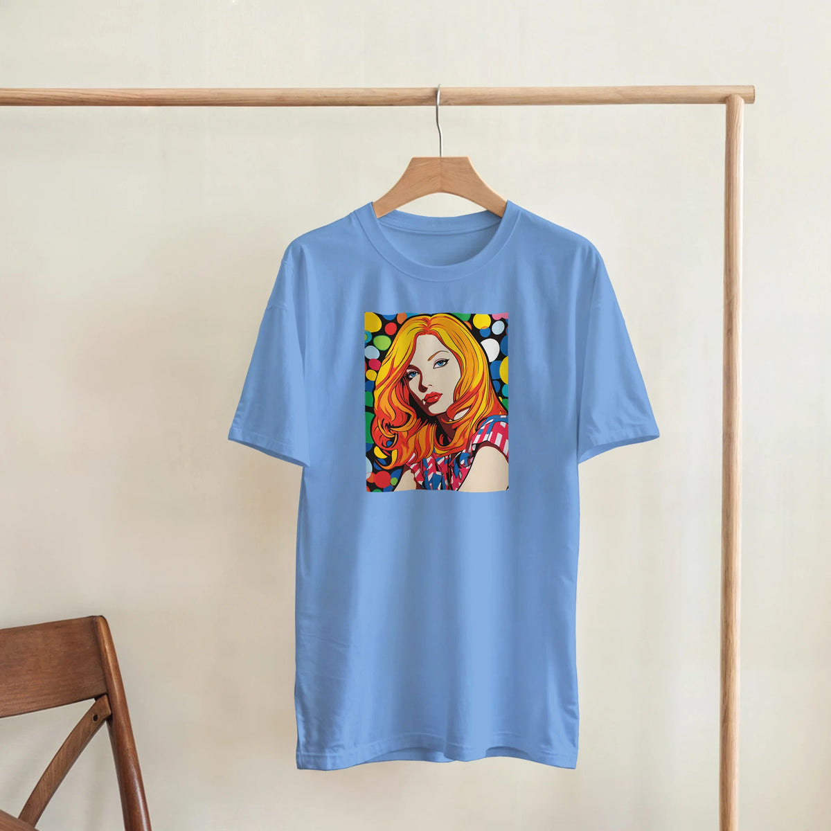 Blue oversized T-shirt with a vibrant pop-art portrait graphic on the chest, hanging on a wooden rack.