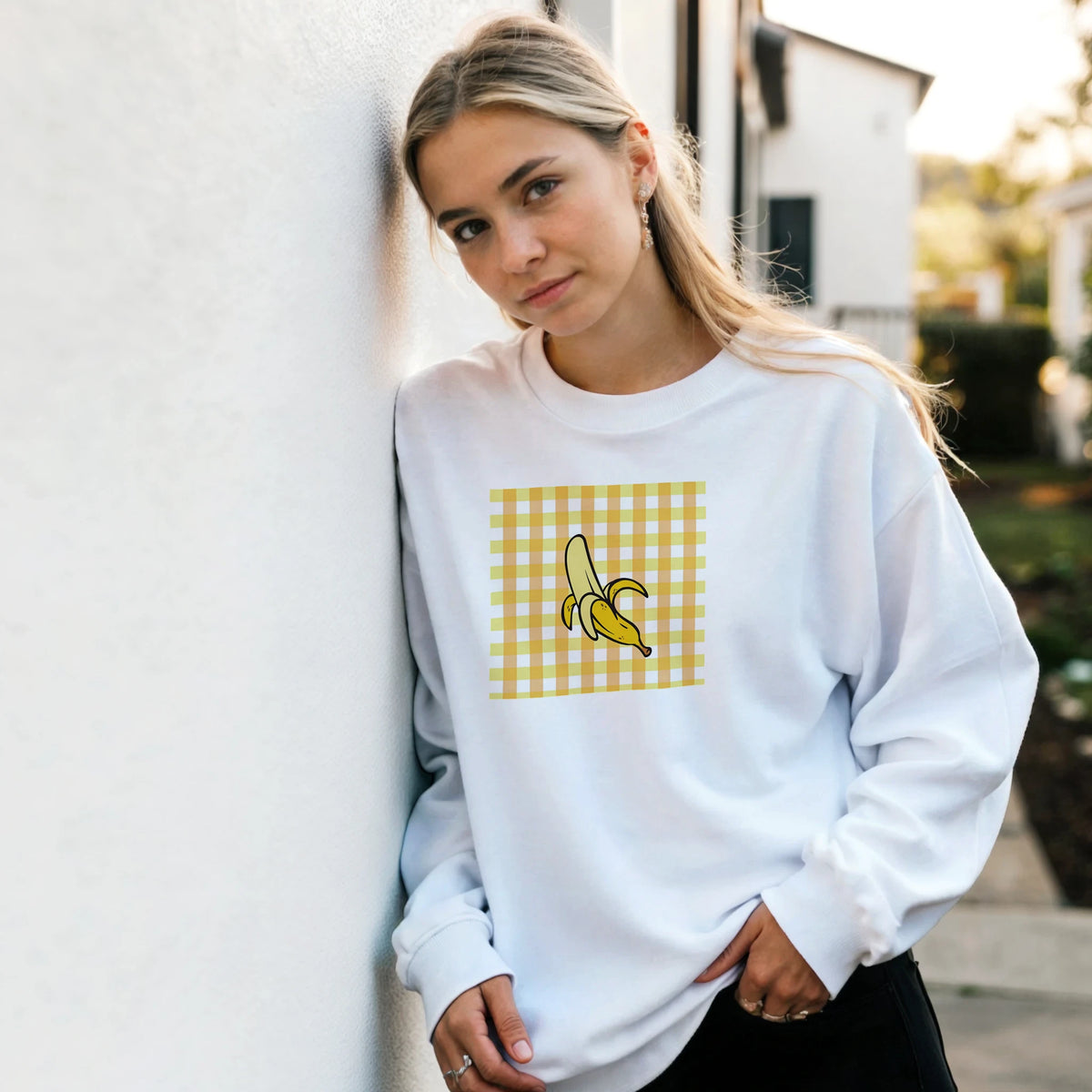 White oversized sweatshirt featuring a playful yellow gingham square graphic with a peeled banana illustration on the chest.