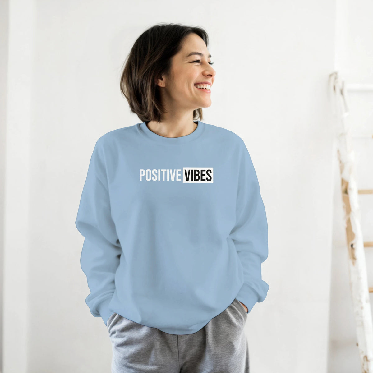 Woman wearing a light blue sweatshirt with the 'POSITIVE VIBES' slogan, casual streetwear look.