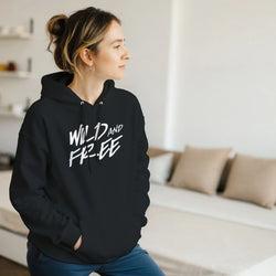 Woman wearing Cute Wild And Free Hoodie in black with white 'Wild And Free' print indoors.