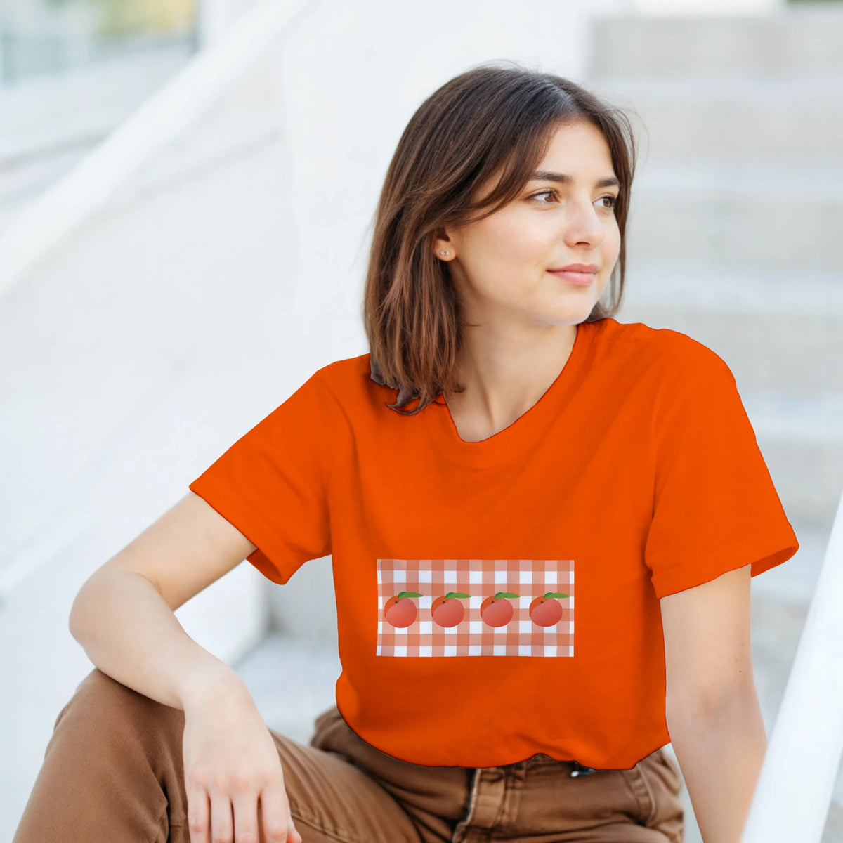 Woman wearing bright orange tee with peach graphic on gingham pocket, summer fruit aesthetic.