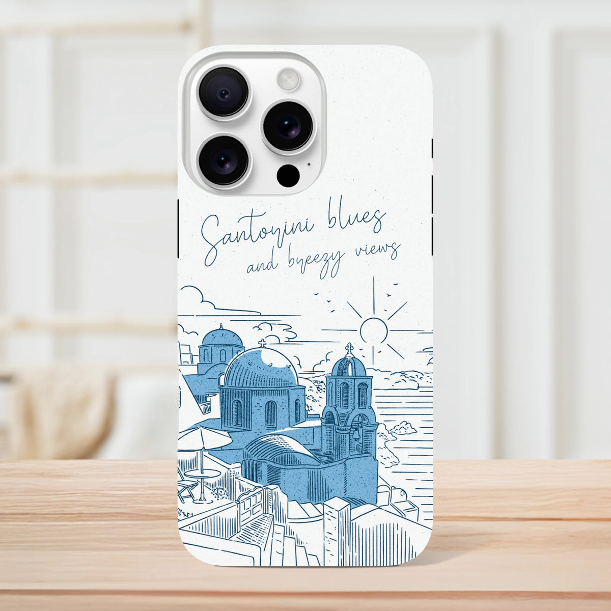 White iPhone case featuring blue Santorini dome illustration and "Santorini blues and breezy views" script text.