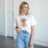 White cotton-blend women's graphic T-shirt with palm trees and a retro sunburst; multicolor accents, sizes S to XL.