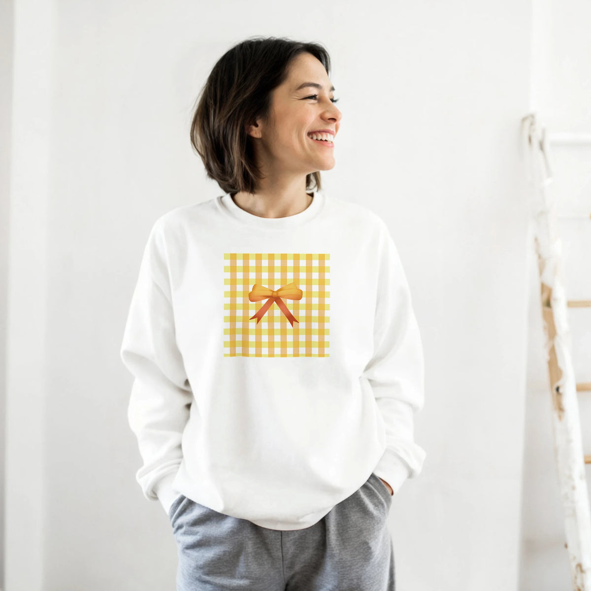 Smiling woman wearing a white sweatshirt with a yellow gingham bow graphic.