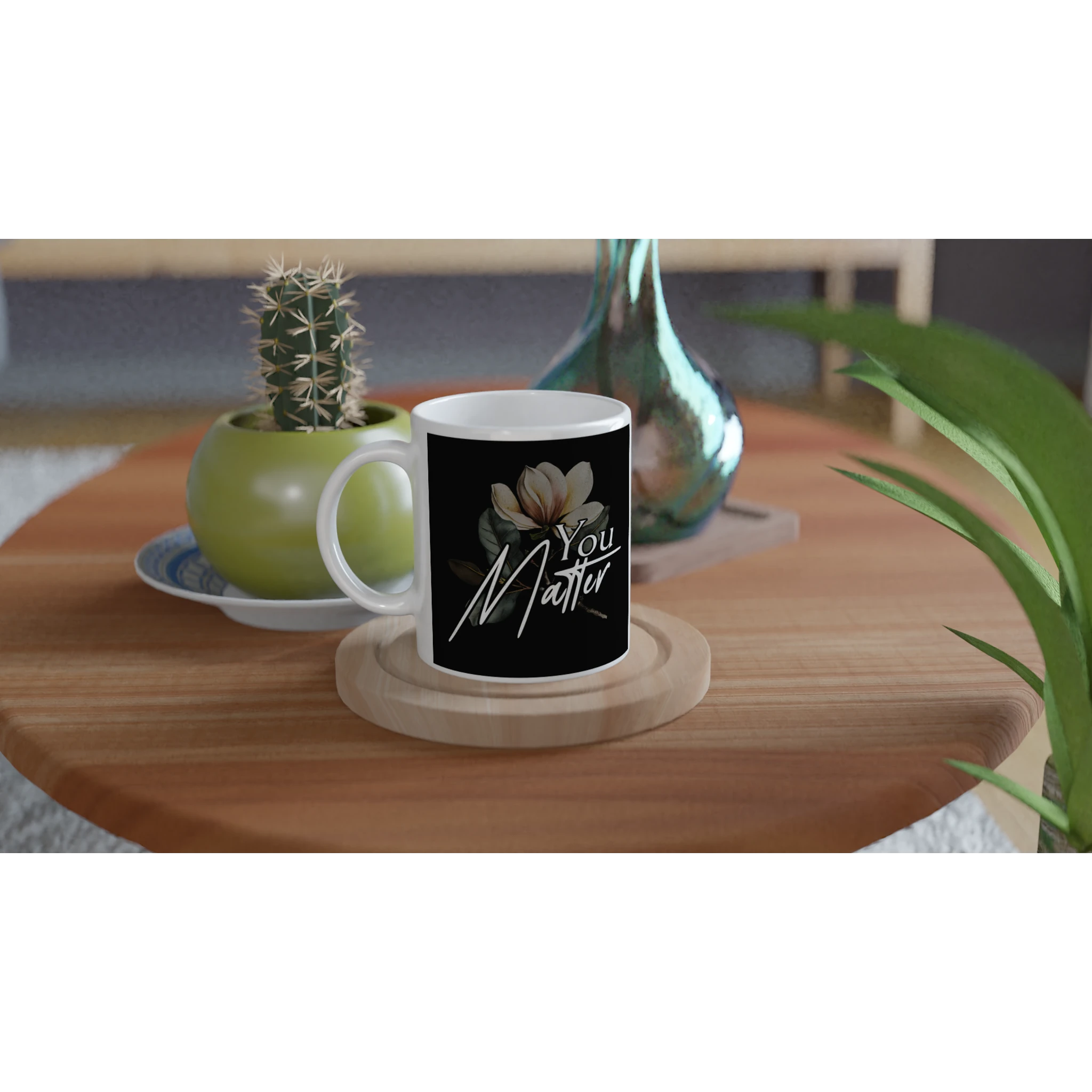 You Matter slogan mug with floral motif on black background; white ceramic on a wooden coaster.