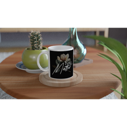 You Matter slogan mug with floral motif on black background; white ceramic on a wooden coaster.