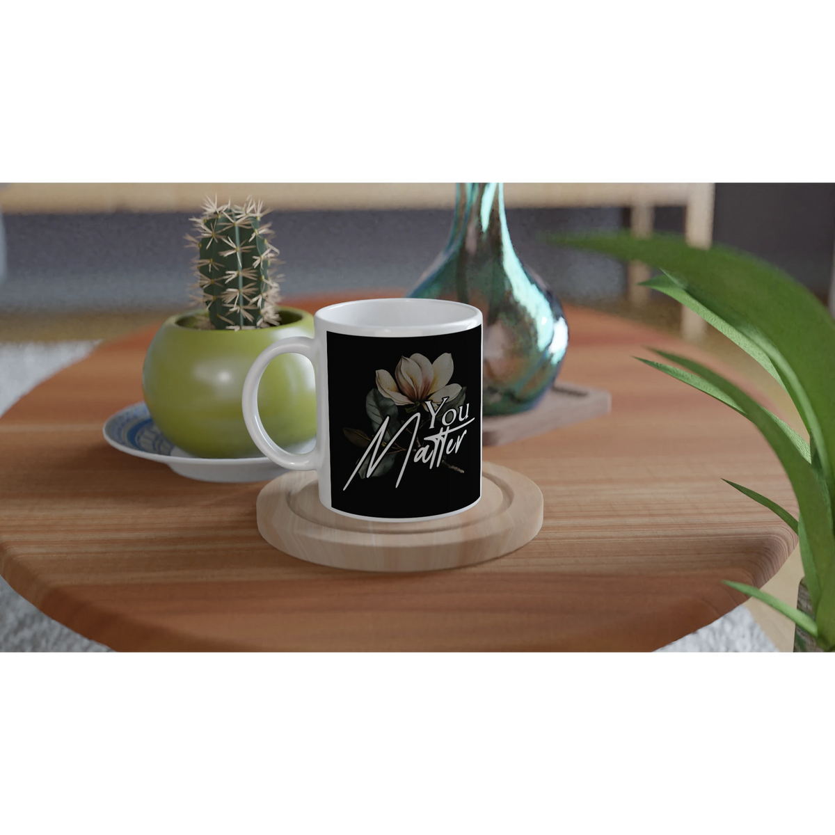 You Matter slogan mug with floral motif on black background; white ceramic on a wooden coaster.