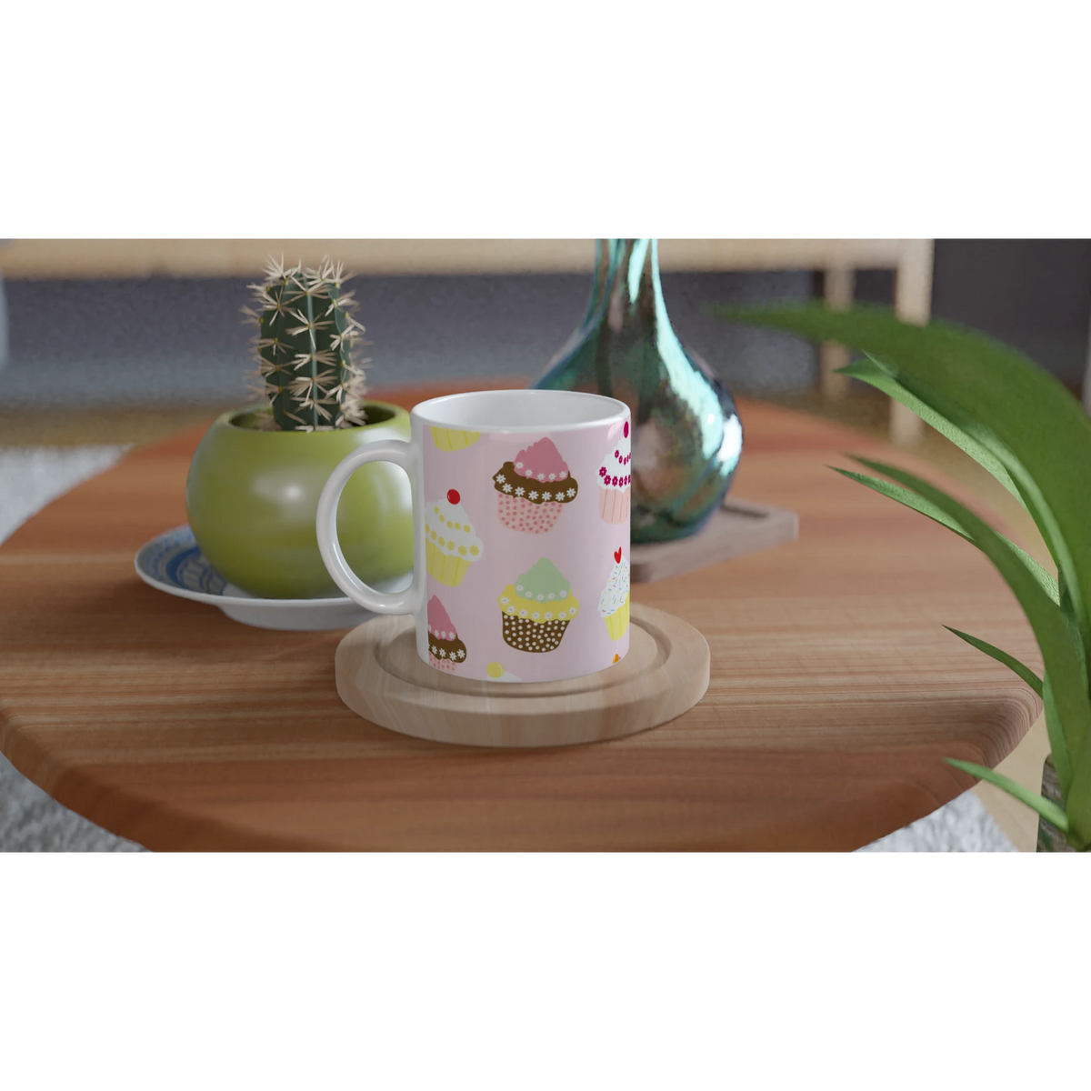 Pastel cupcake ceramic mug with kawaii print sits on a wooden table beside a cactus plant.