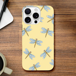 Yellow dragonfly phone case featuring a blue insect pattern on a pale background, shown protecting an iPhone on a wooden desk.