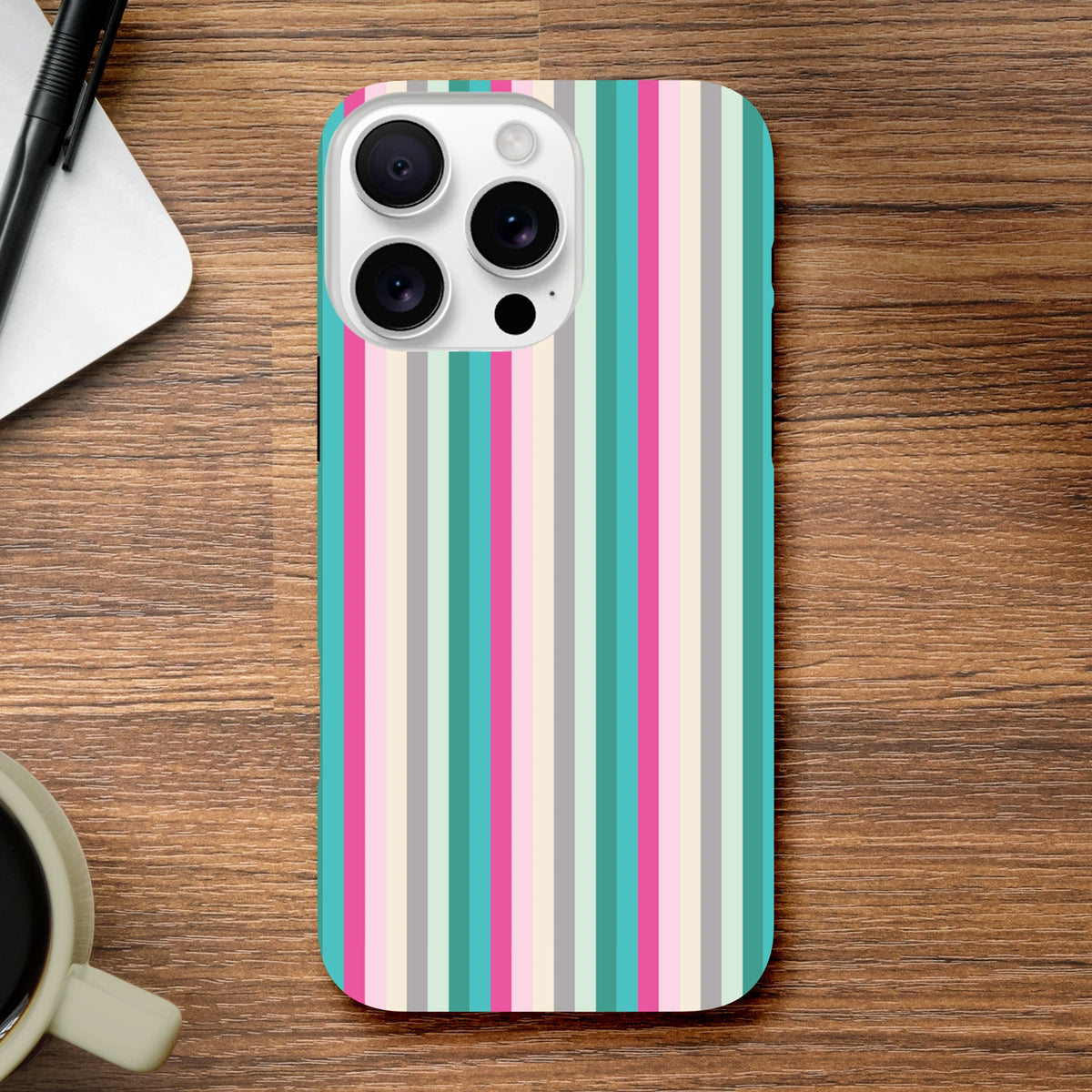 Retro pink and aqua vertical stripe tough iPhone case on wooden desk with coffee and pen.