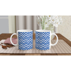 Pair of blue wavy stripe ceramic mugs with retro geometric design on a checkered placemat beside wooden spoons.