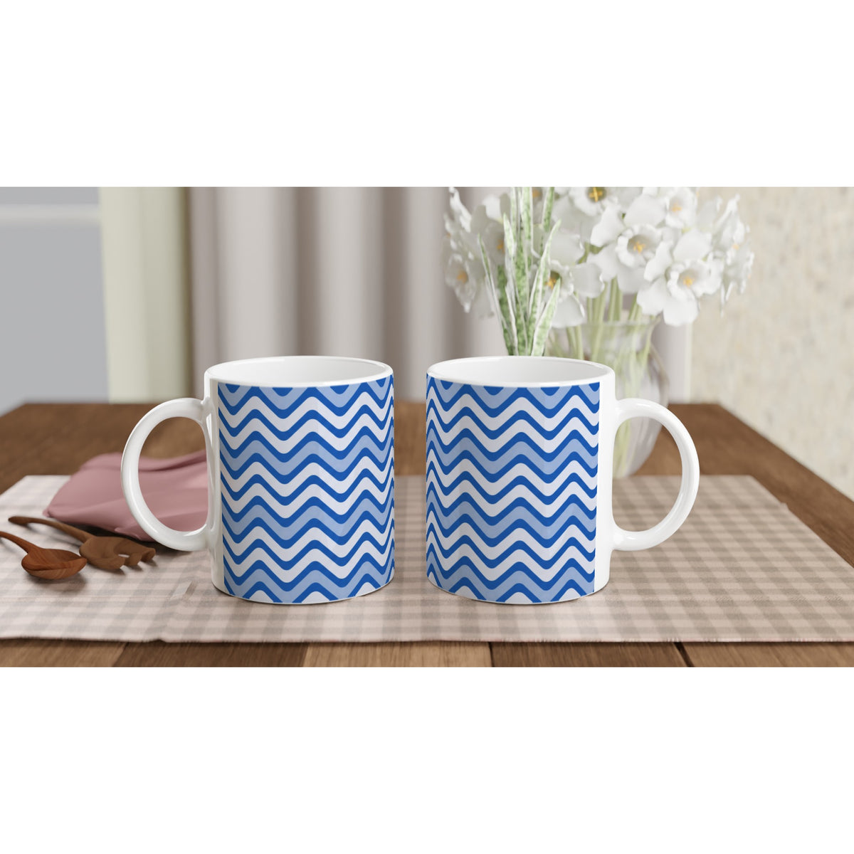 Pair of blue wavy stripe ceramic mugs with retro geometric design on a checkered placemat beside wooden spoons.