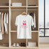 White t-shirt with 'Sweet Cherries' design hanging in a wardrobe with shoes and boxes below.
