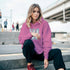 Woman wearing pink cotton-blend Washington University hoodie sits on outdoor steps.
