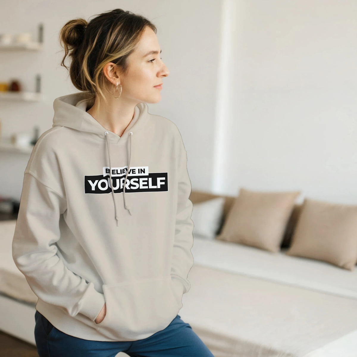 Woman in beige Believe In Yourself hoodie with bold slogan, casual streetwear look.