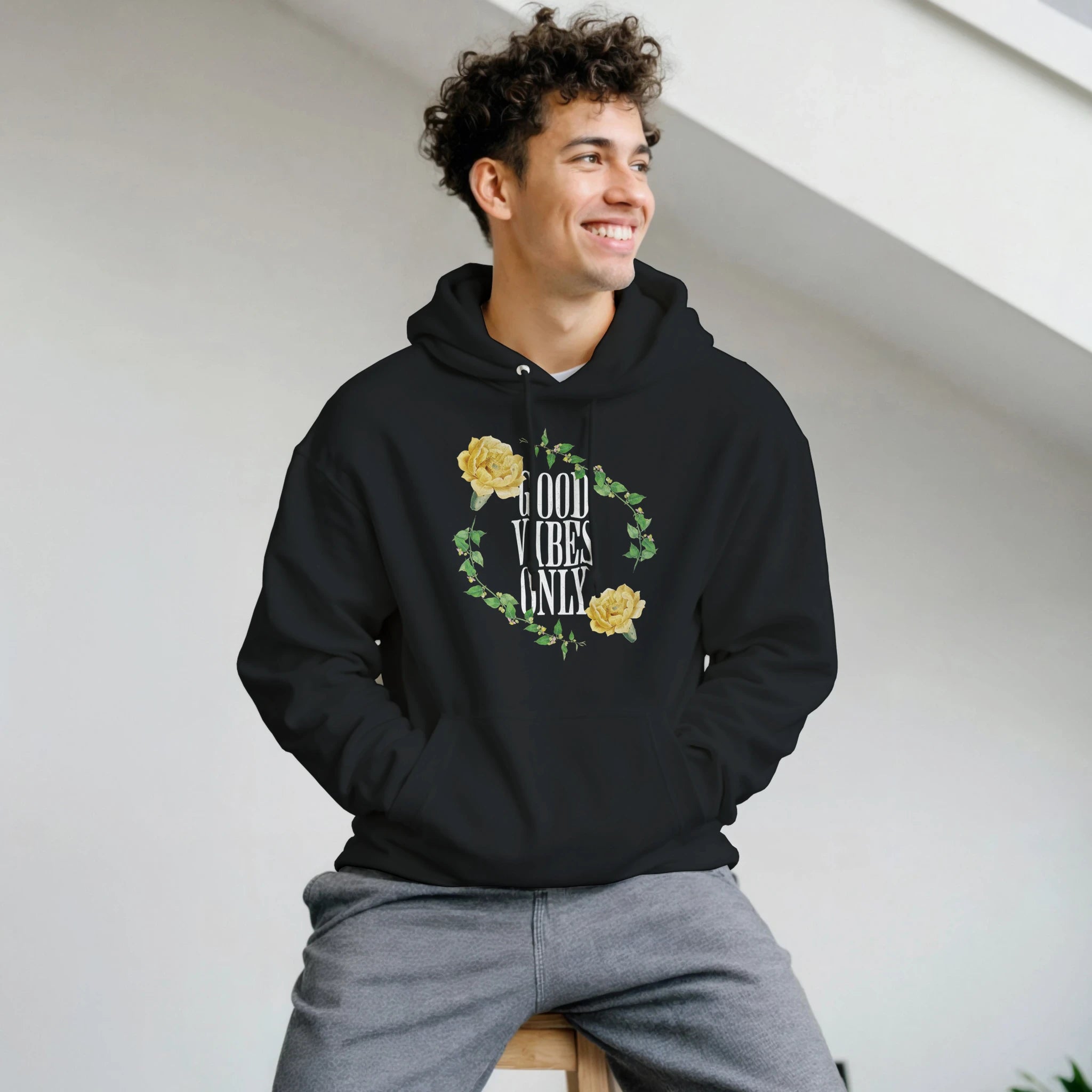 Man wearing black Good Vibes Only graphic hoodie with floral wreath design and front pouch pocket.