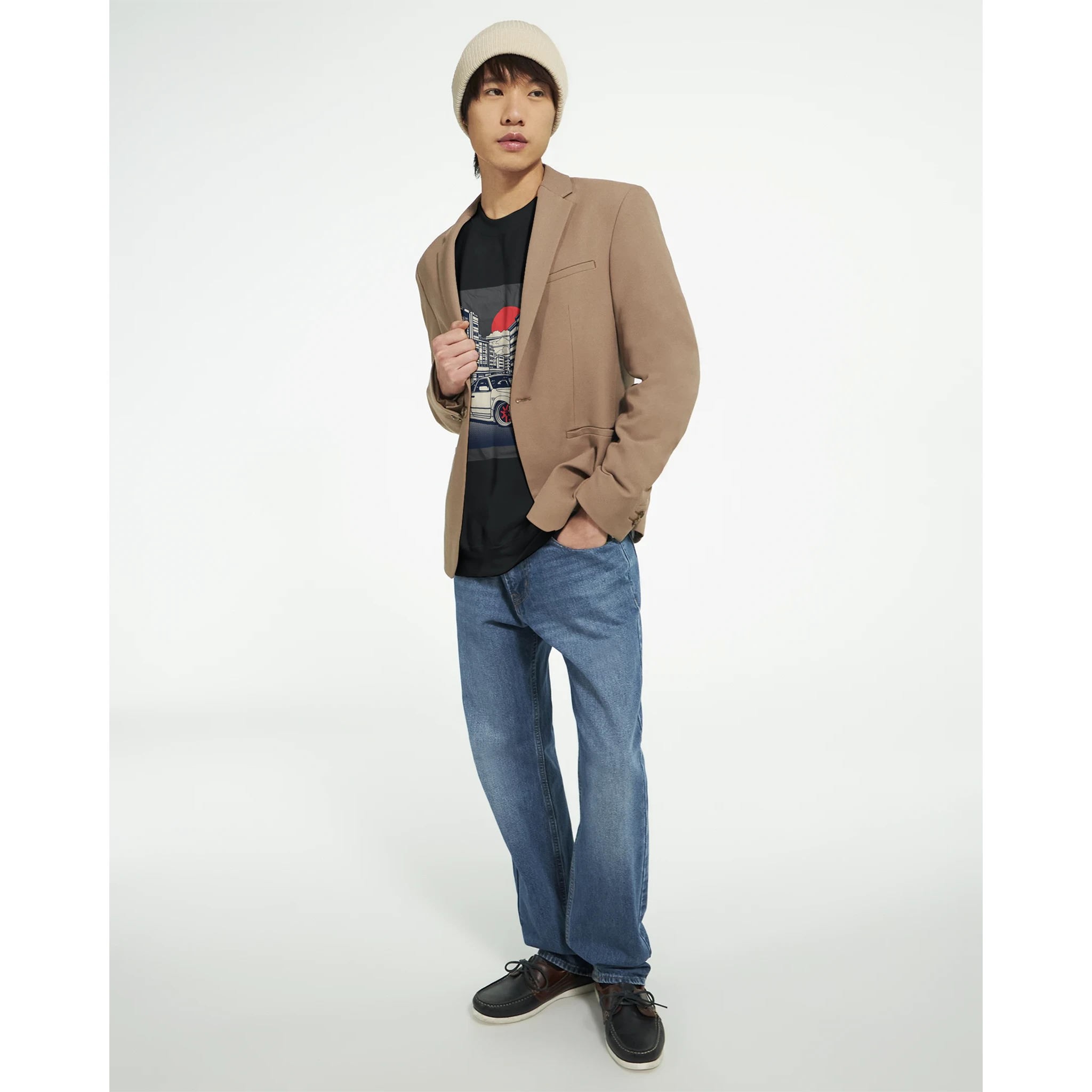 Male model wearing tan blazer, black graphic T-shirt, blue jeans, and beige beanie.