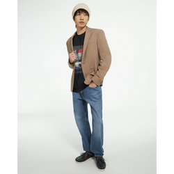 Male model wearing tan blazer, black graphic T-shirt, blue jeans, and beige beanie.