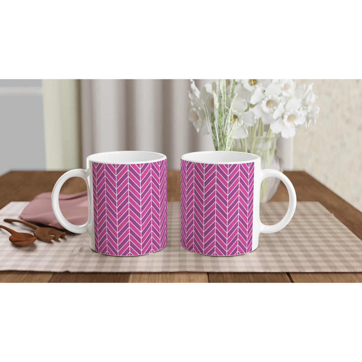 Two pink and purple herringbone ceramic mugs with retro geometric patterns on a checkered placemat with wooden spoons.