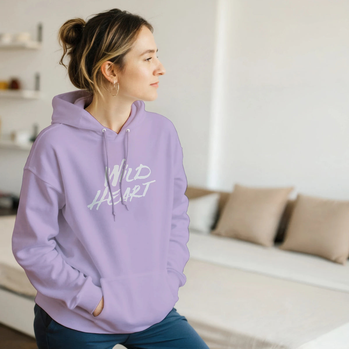 Woman in lavender hoodie with Wild Heart slogan, indoors, casual streetwear vibe.