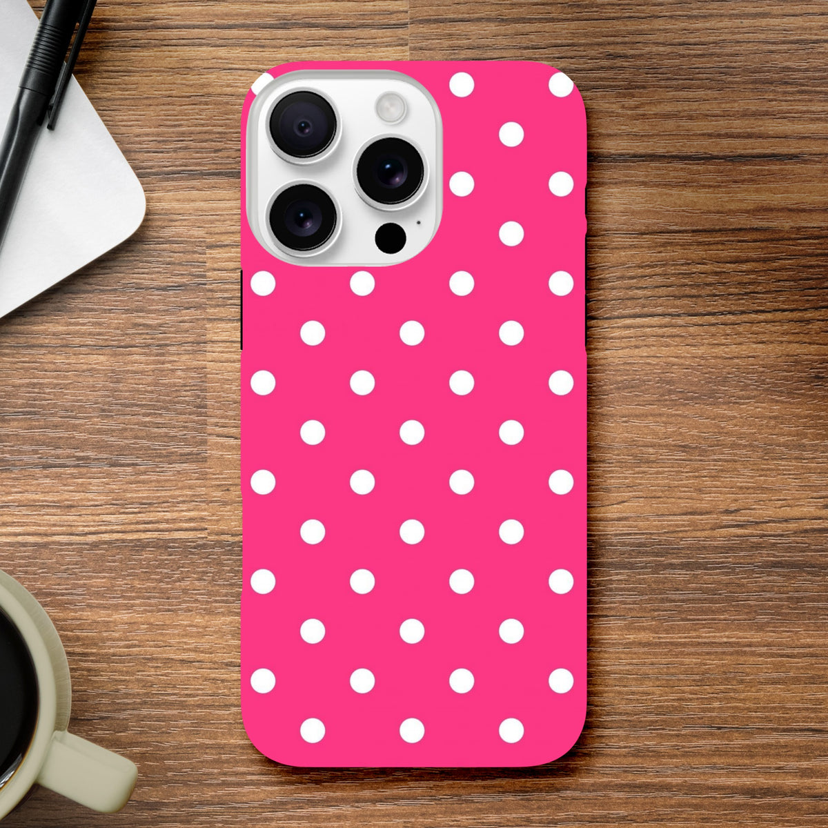 Hot pink and white polka dot tough iPhone case with rugged dual-layer protection and shock-absorbing TPU on a wooden desk.