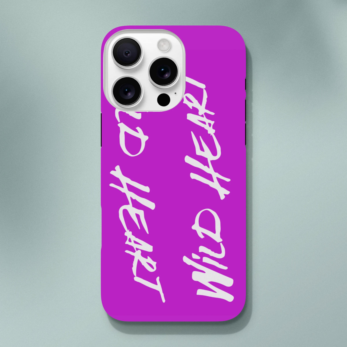 Vivid purple iPhone case with white "Wild Heart" brush script text. Tough streetwear phone cover with shock-absorbing protection for urban drops.