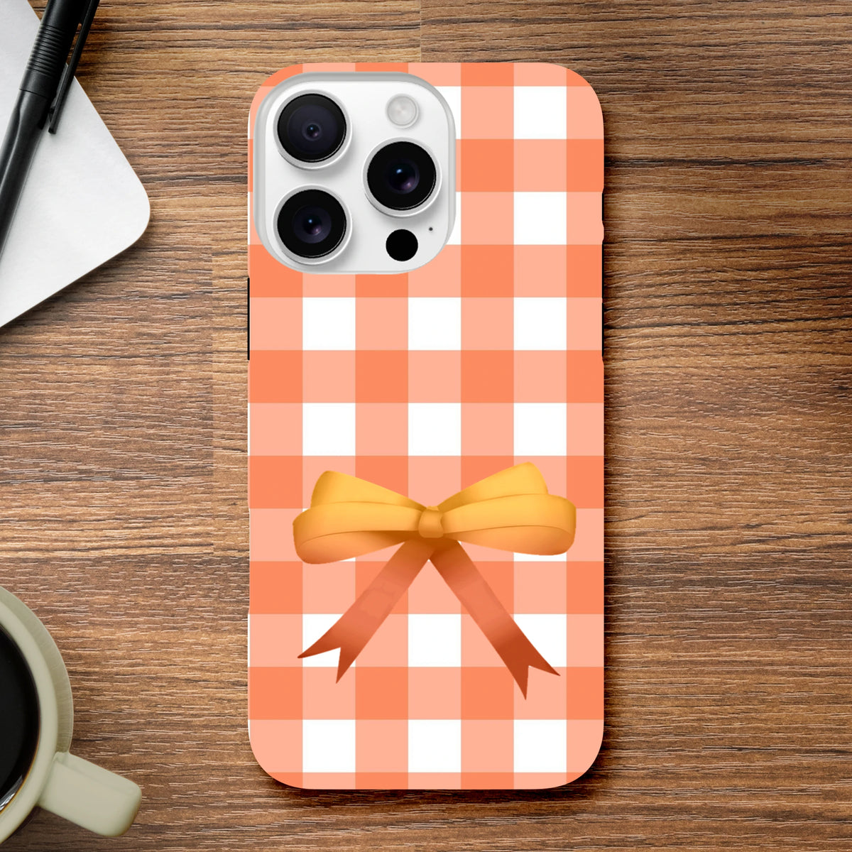 Impact-resistant orange gingham iPhone case featuring a cute yellow coquette bow design for sturdy daily protection.