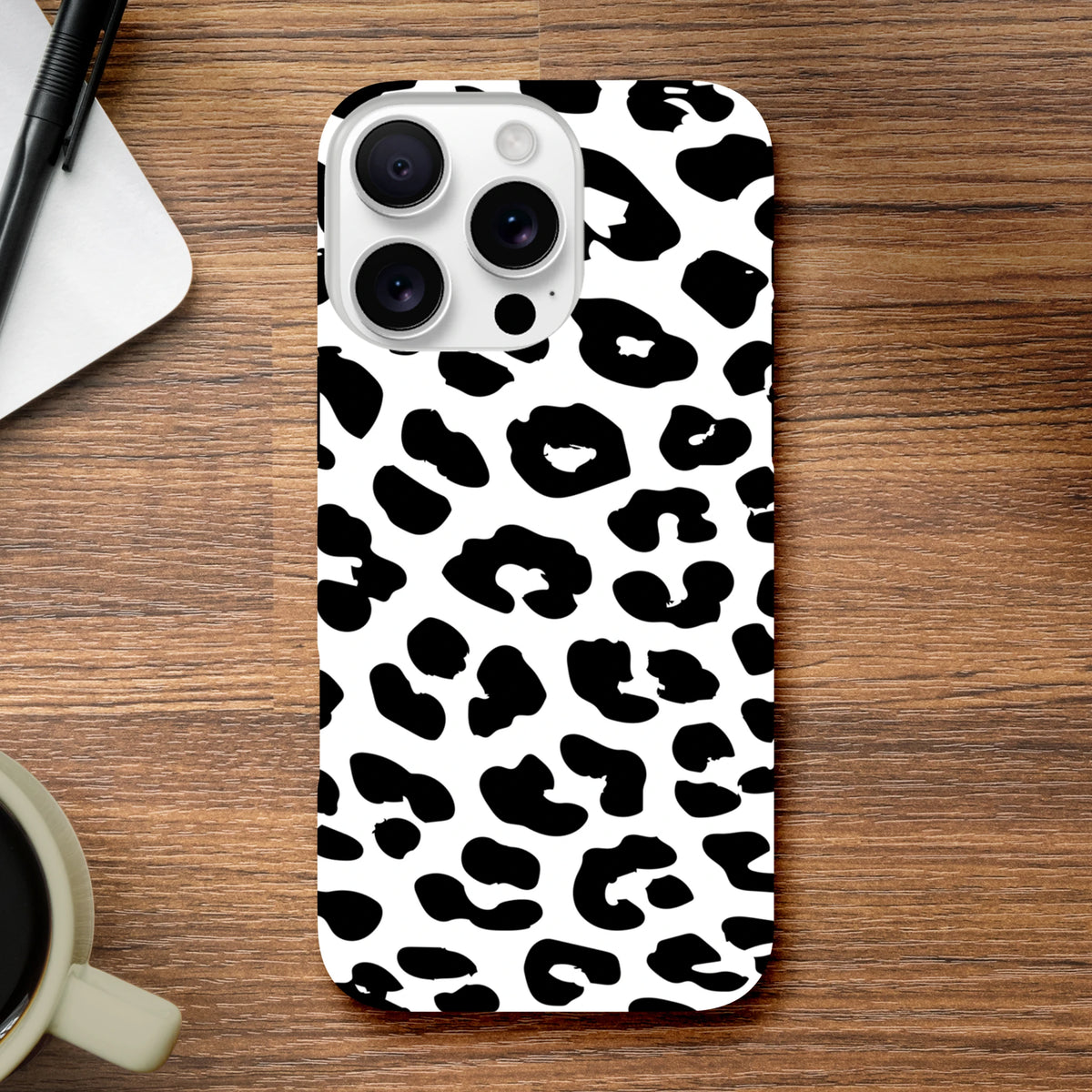 Black and white snow leopard print tough iPhone case on wooden desk, offering shock-absorbing protection with a stylish animal pattern design.