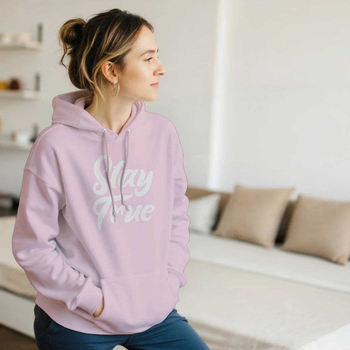 Profile of a woman wearing a pastel pink Stay True hoodie with white slogan and front pouch pocket.