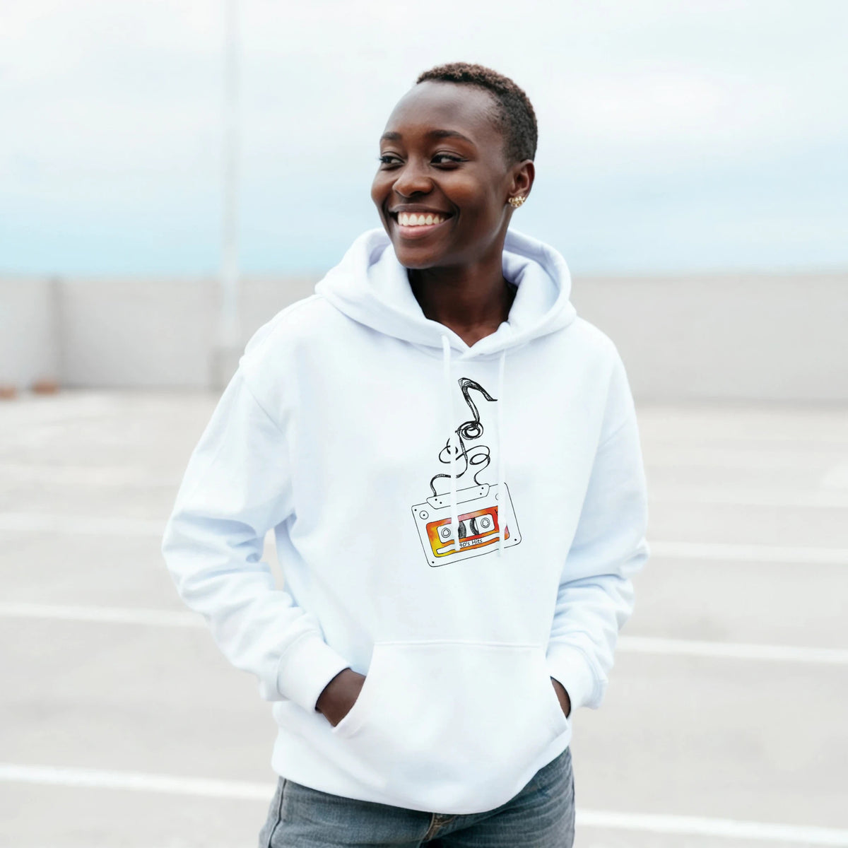 Smiling person wearing a light hoodie with a retro cassette tape graphic.