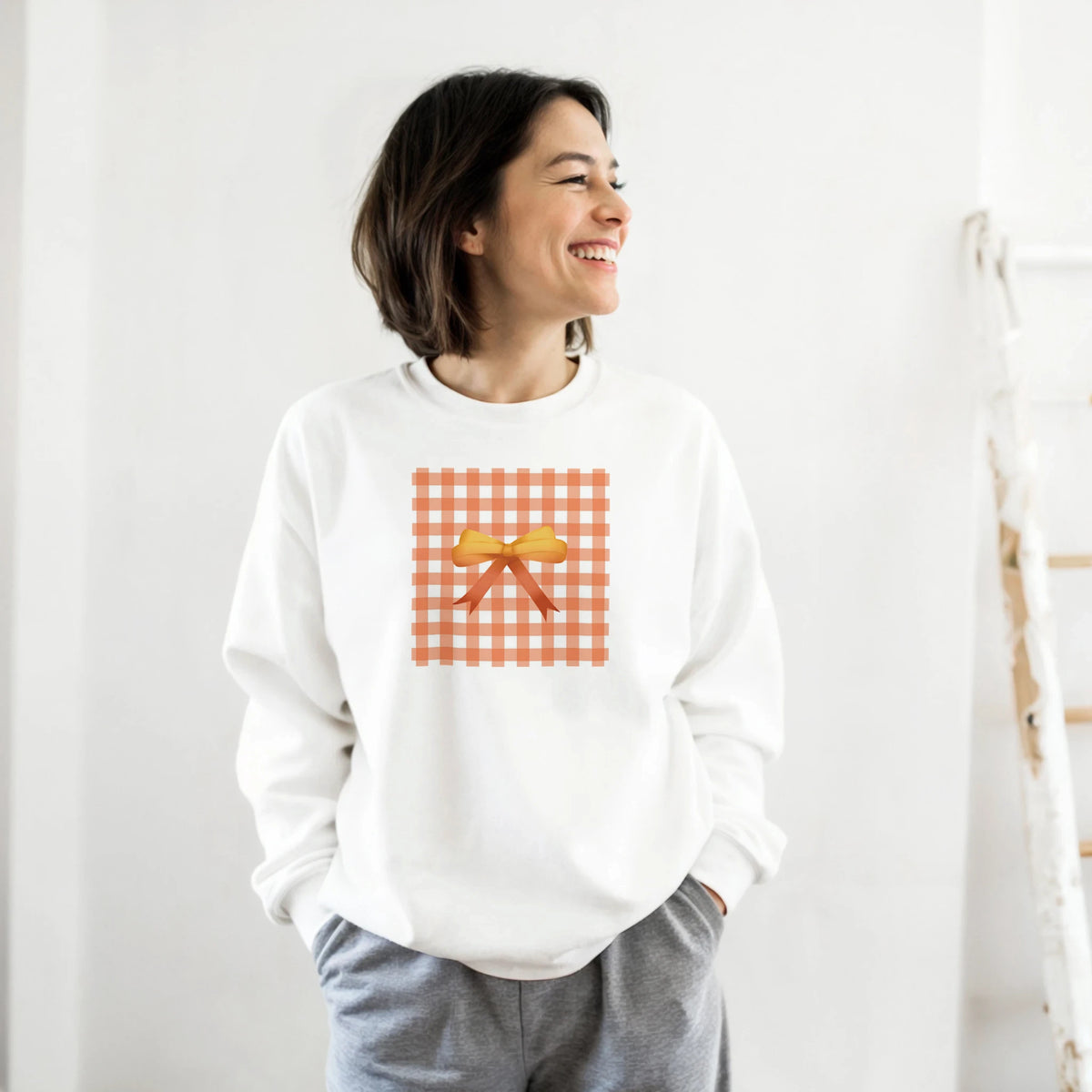 White sweatshirt featuring an orange gingham square graphic with a yellow coquette bow, perfect for cute street-style layering.