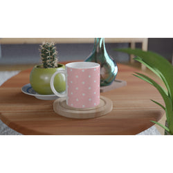 Pastel pink and white polka dot ceramic mug with a comfy handle, sitting on a wooden coaster beside a small cactus.