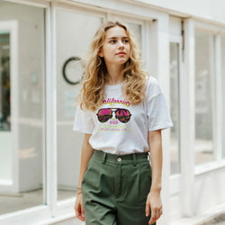 Woman wearing a white Y2K California Beach T‑Shirt with retro sunglasses graphic.