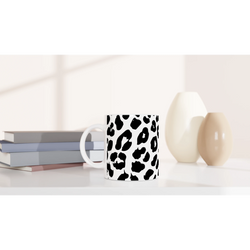 White leopard-print mug with bold black spots on a desk beside books and a lamp.