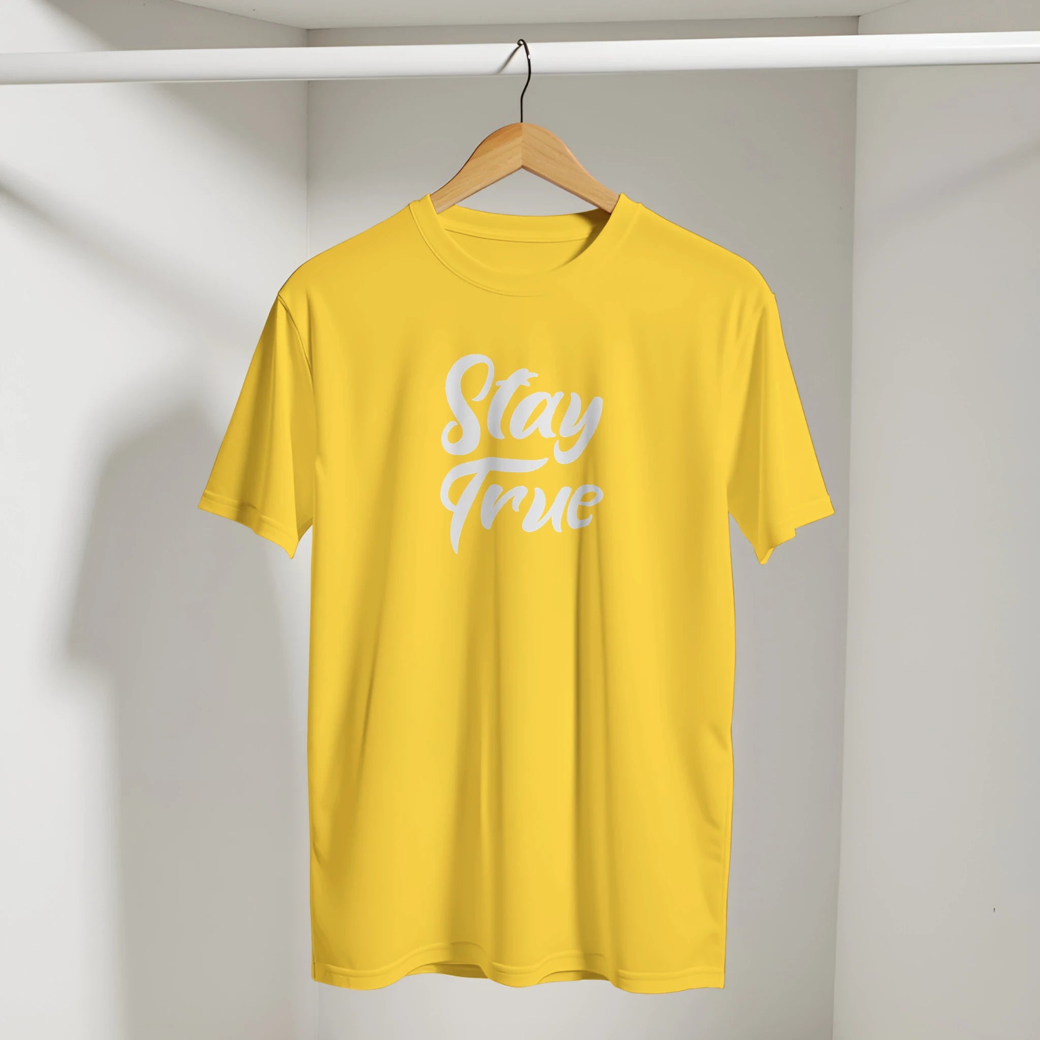 Yellow Cute Stay True T-shirt on wooden hanger in closet with white retro slogan.