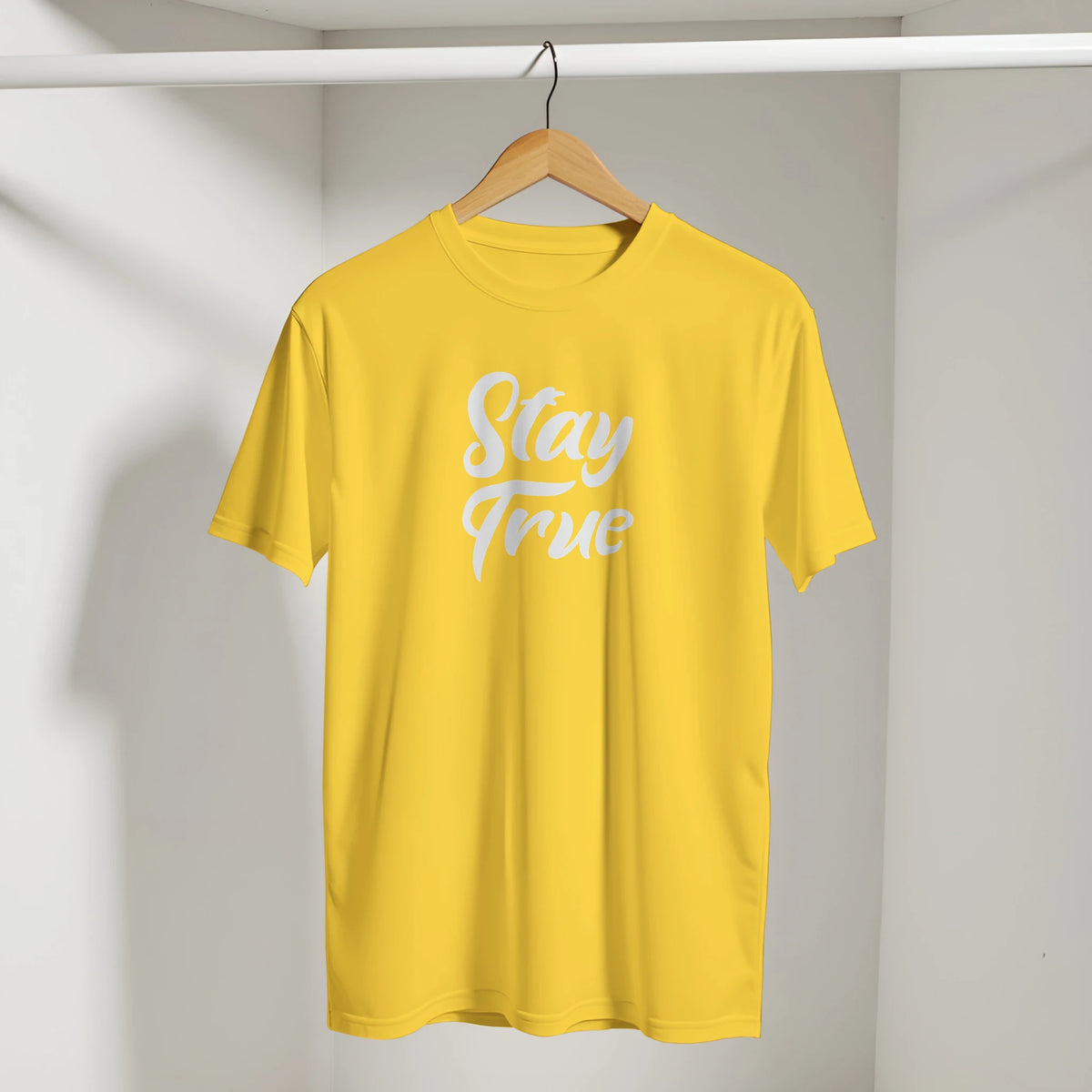 Yellow Cute Stay True T-shirt on wooden hanger in closet with white retro slogan.
