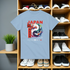 Light blue t-shirt with Japanese design on a wooden shelf with shoes and plants.