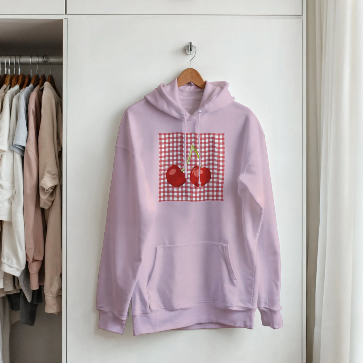 Lavender retro hoodie featuring a red cherry graphic on a gingham patch, hanging in a closet.