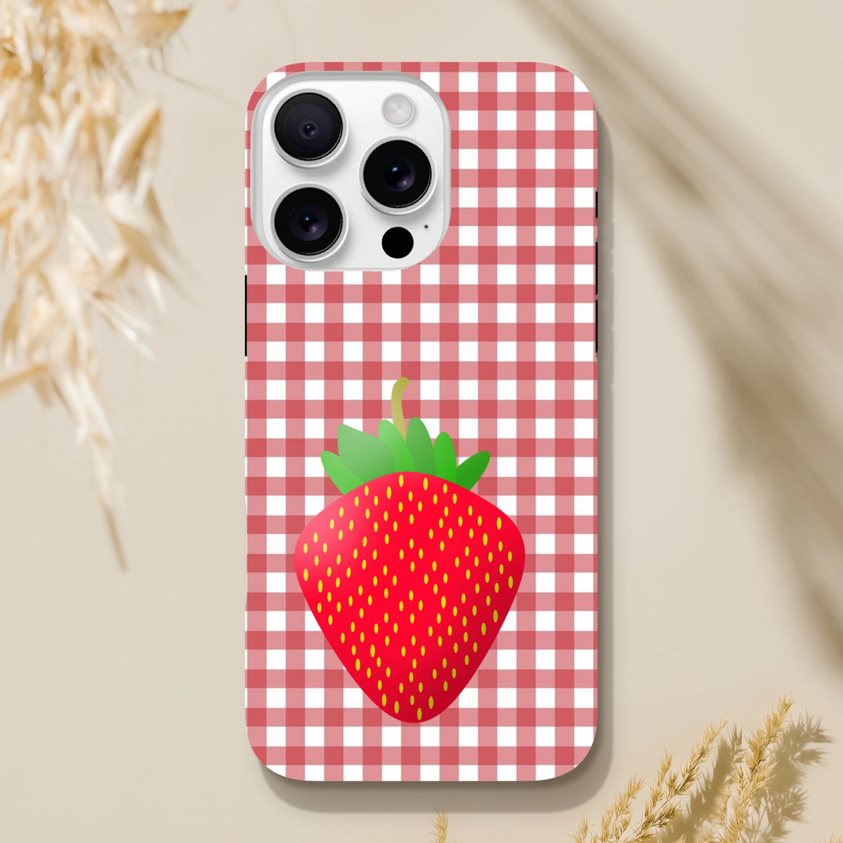 Red gingham iPhone case featuring a large cute strawberry illustration and tough drop protection for models 13-16.