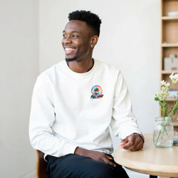 Man wearing a white crewneck sweatshirt featuring a colorful Urban Palm Trees Full Send graphic on the left chest.
