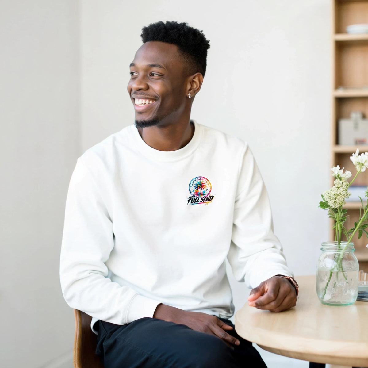Man wearing a white crewneck sweatshirt featuring a colorful Urban Palm Trees Full Send graphic on the left chest.