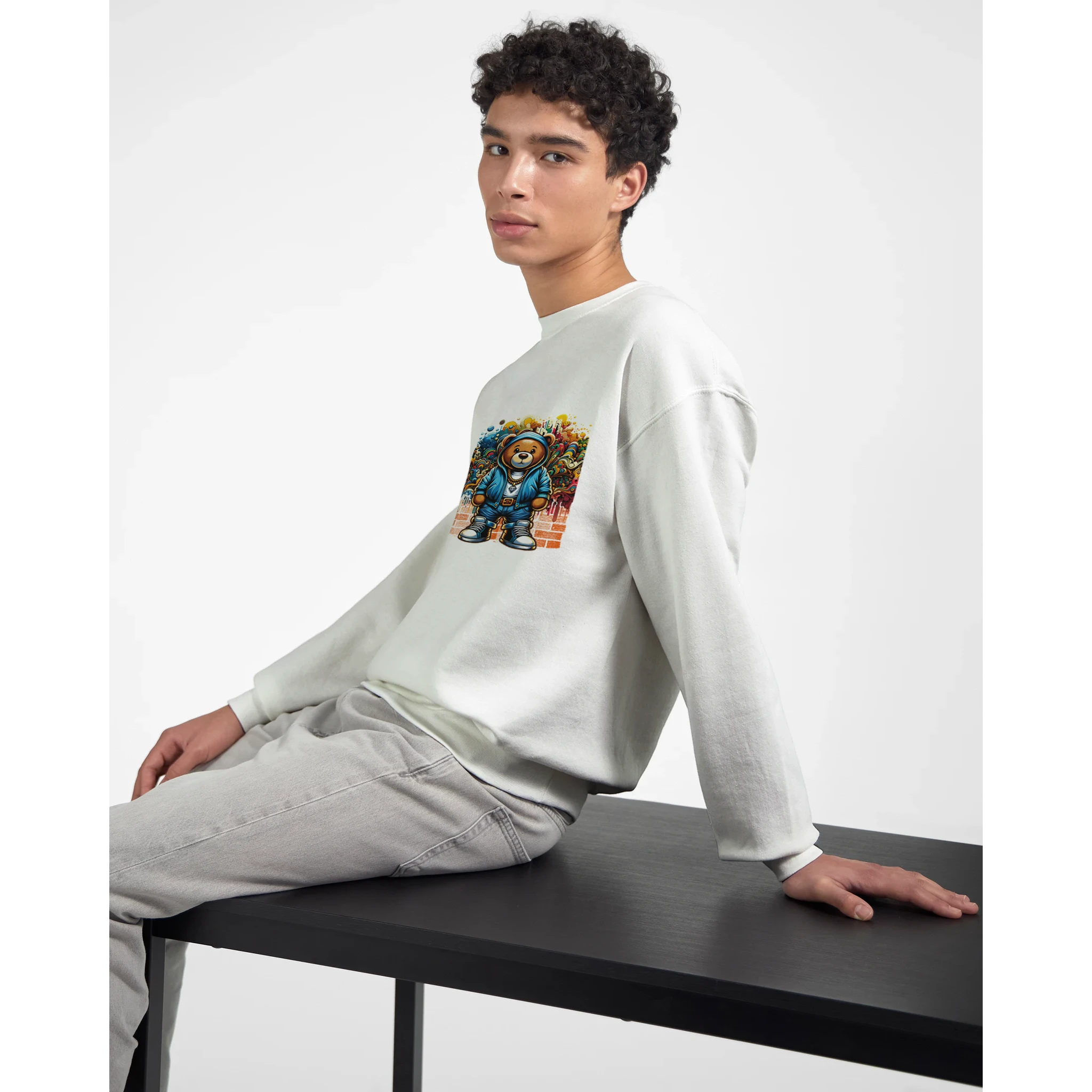 Man wearing white Urban Teddy Bear graphic sweatshirt with colorful bear artwork, seated at a table.