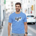 Man wearing Hype Men's Graphic T-Shirt, soft cotton blend blue tee with white brush-stroke logo on city street.